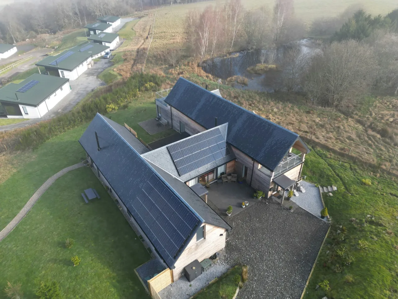 Slate roofs with solar panels on a timber-clad home beside a pond