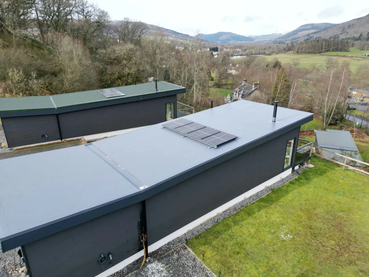 Finished single-ply flat roof with solar panels on a timber-clad lodge