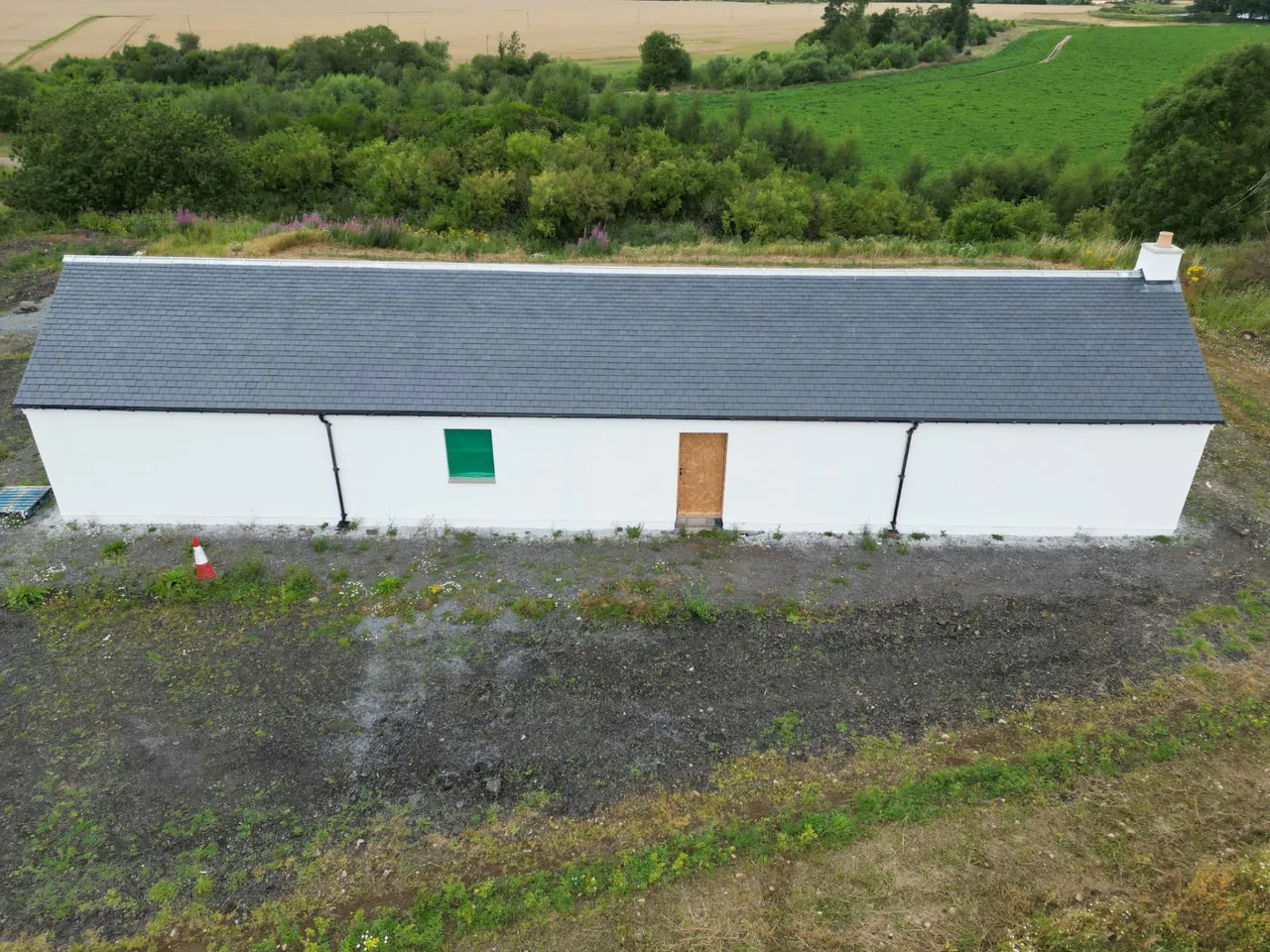 Aerial view of a new slate roof on a long white rendered cottage