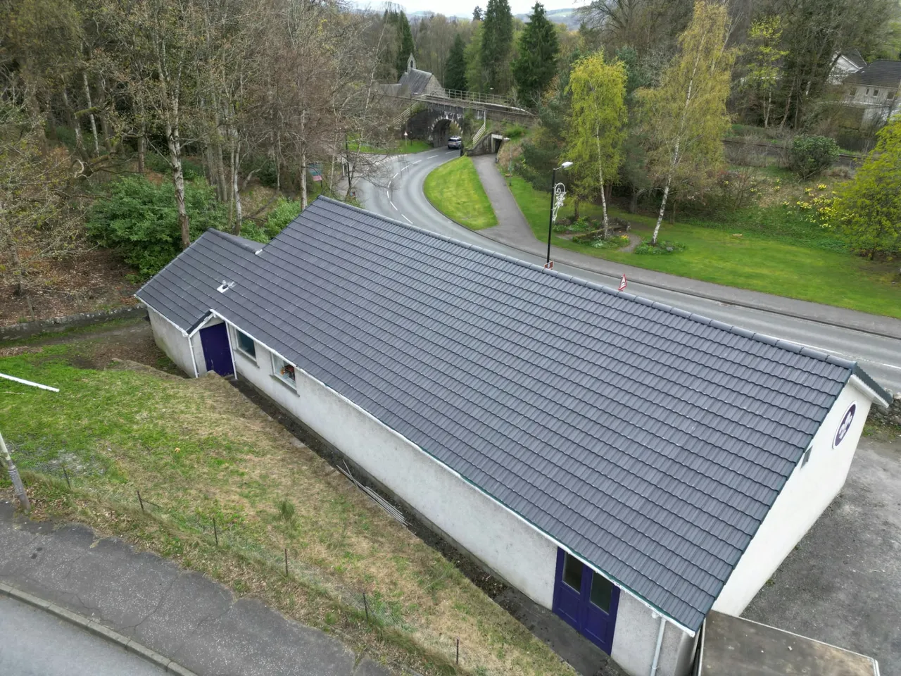 Aerial view of a long community hall with a newly tiled roof beside a village road